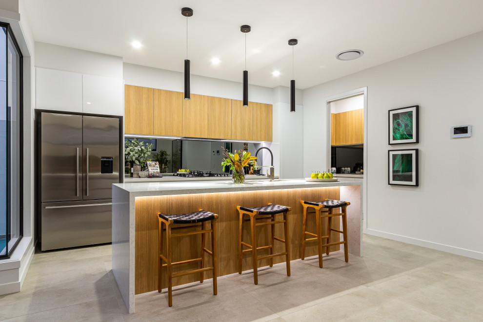 Foto på ett stort funkis grå l-kök, med en undermonterad diskho, släta luckor, skåp i mellenmörkt trä, spegel som stänkskydd, rostfria vitvaror, en köksö och grått golv