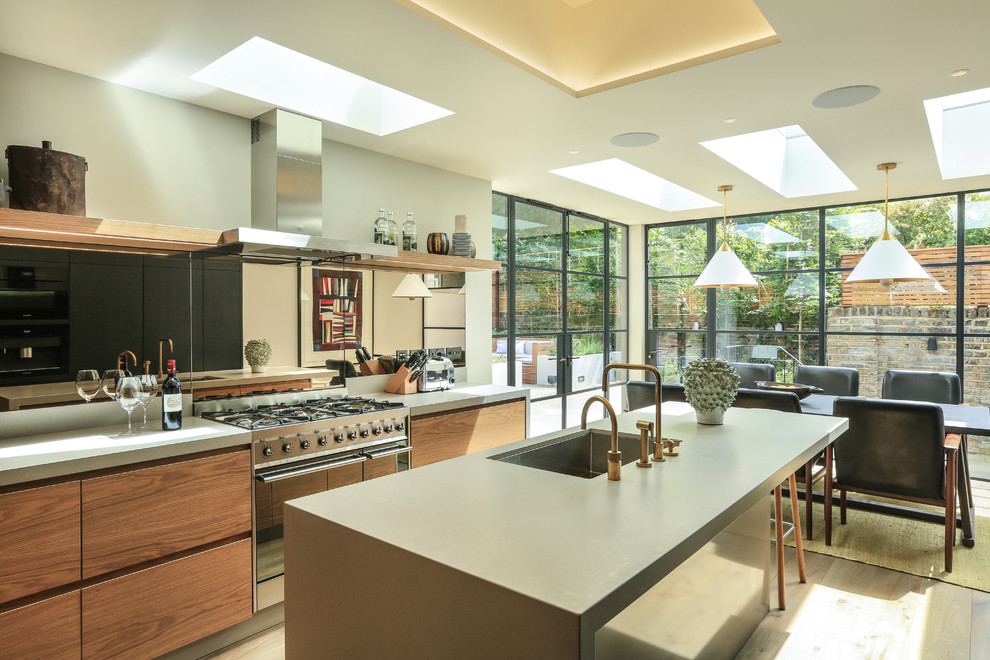 Moderne Wohnküche mit Unterbauwaschbecken, flächenbündigen Schrankfronten, hellbraunen Holzschränken, Küchengeräten aus Edelstahl, braunem Holzboden, Kücheninsel, braunem Boden und grauer Arbeitsplatte in London