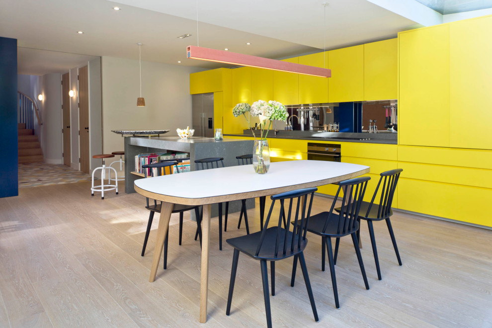 На фото: большая параллельная кухня в современном стиле с обеденным столом, плоскими фасадами, желтыми фасадами, зеркальным фартуком, техникой под мебельный фасад, островом, бежевым полом и серой столешницей