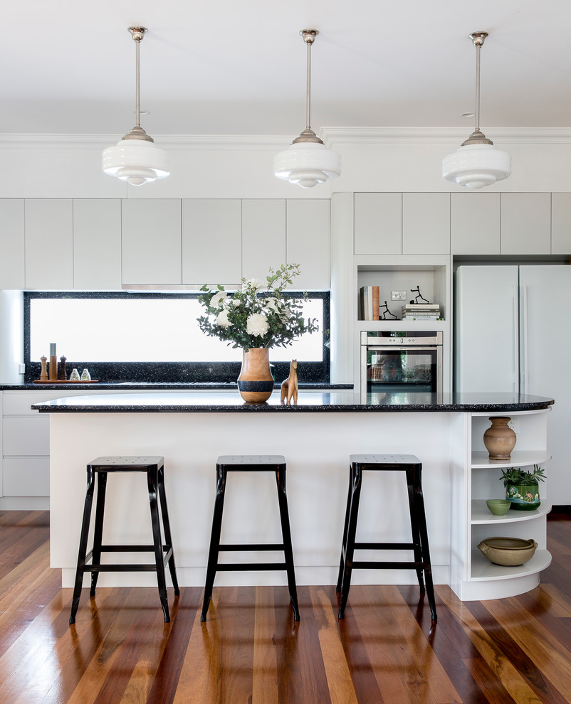Foto de cocinas en L contemporánea de tamaño medio con puertas de armario blancas, salpicadero negro, suelo de madera en tonos medios y una isla