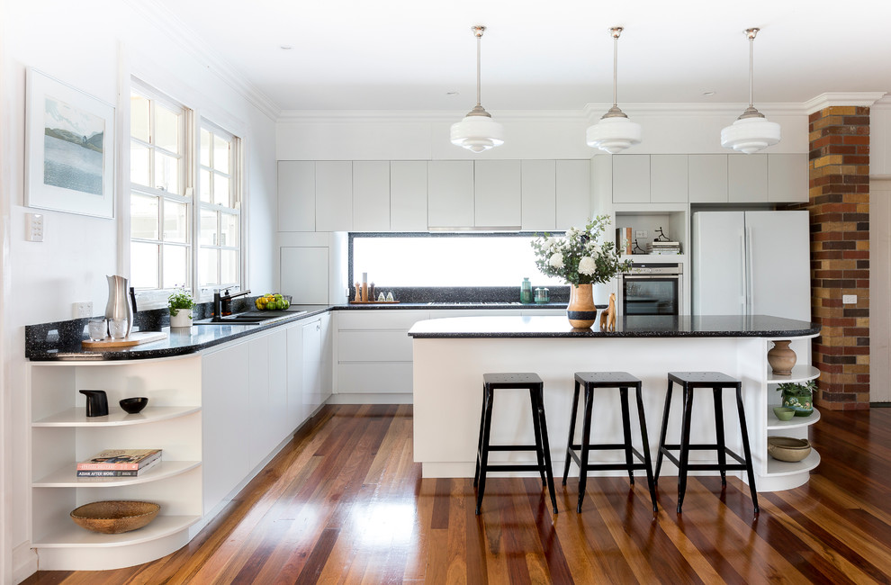 Stilmix Küche in L-Form mit weißen Schränken, Küchenrückwand in Schwarz, braunem Holzboden und Kücheninsel in Brisbane
