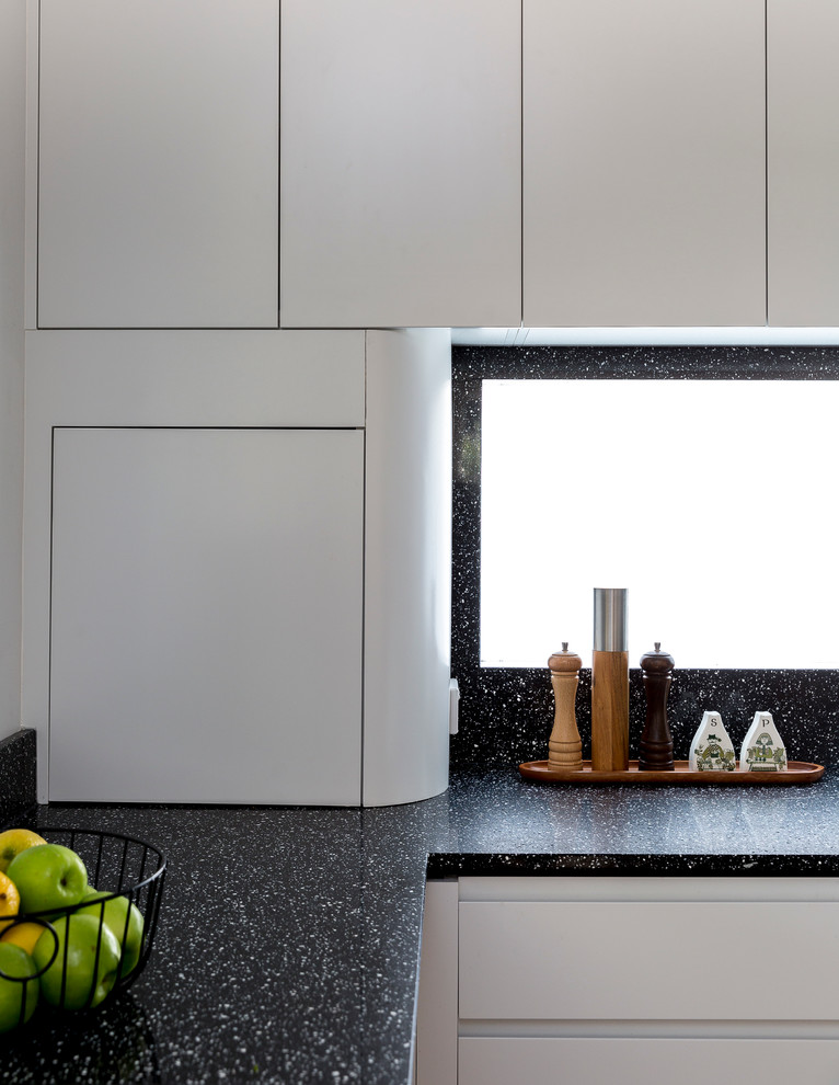 Exemple d'une cuisine tendance en L avec des portes de placard blanches, un plan de travail en terrazzo, une crédence noire, un sol en bois brun et îlot.