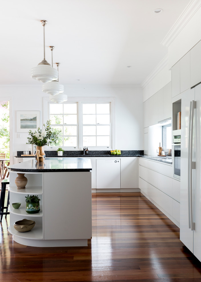 Klassische Küche in L-Form mit Doppelwaschbecken, weißen Schränken, Küchenrückwand in Schwarz, braunem Holzboden und Kücheninsel in Brisbane