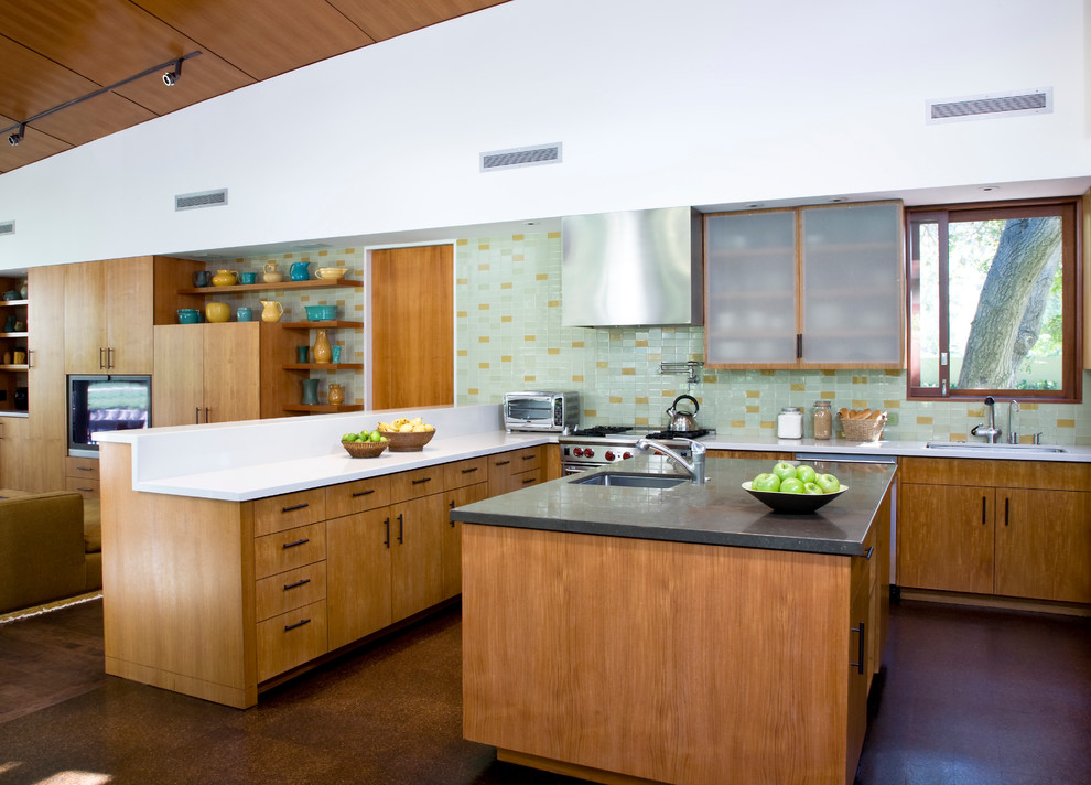 Стильный дизайн: п-образная кухня-гостиная в современном стиле с плоскими фасадами, фасадами цвета дерева среднего тона и зеленым фартуком - последний тренд