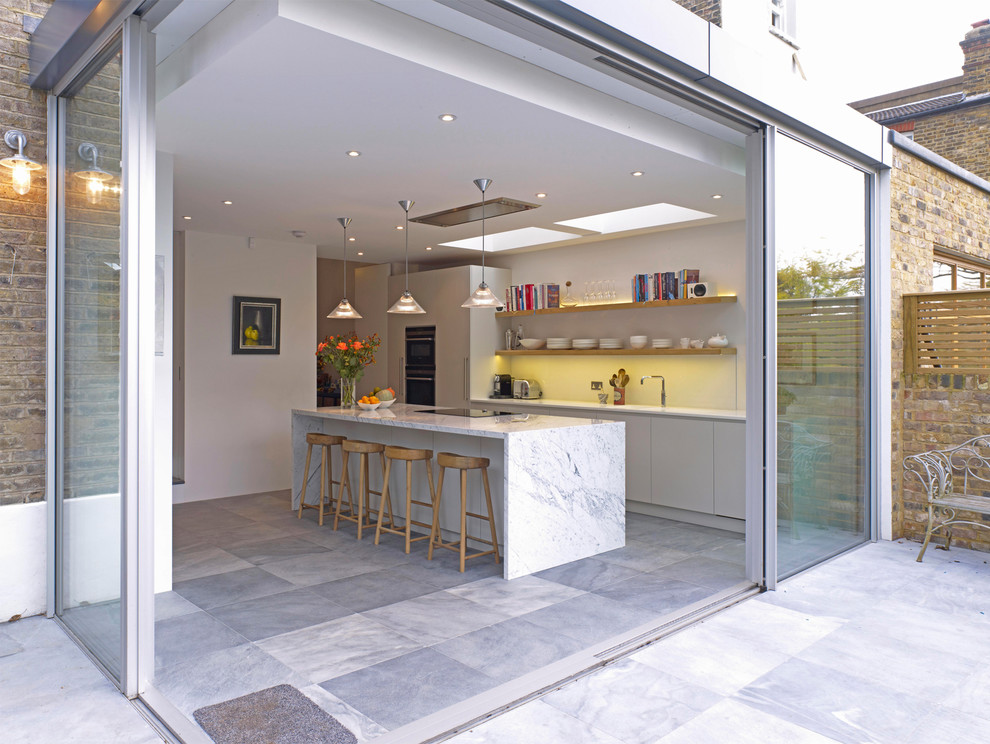 ロンドンにあるお手頃価格の広いコンテンポラリースタイルのおしゃれなキッチン (フラットパネル扉のキャビネット、グレーのキャビネット、大理石カウンター、白いキッチンパネル、ガラス板のキッチンパネル、黒い調理設備、セラミックタイルの床) の写真