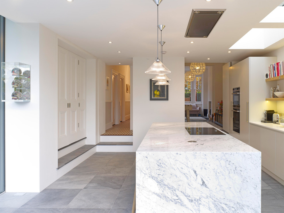 Photo of a large contemporary galley kitchen in London with flat-panel cabinets, grey cabinets, marble worktops, white splashback, glass sheet splashback, black appliances, ceramic flooring and an island.