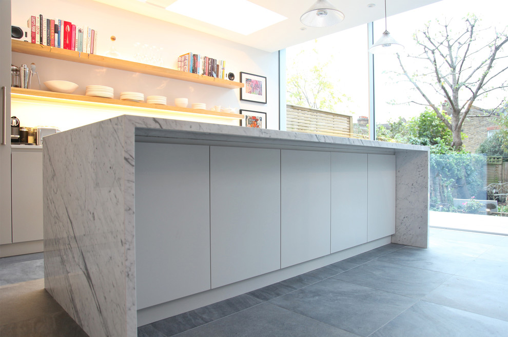 This is an example of a large contemporary galley open plan kitchen in London with flat-panel cabinets, grey cabinets, marble worktops, white splashback, glass sheet splashback, black appliances, ceramic flooring and an island.