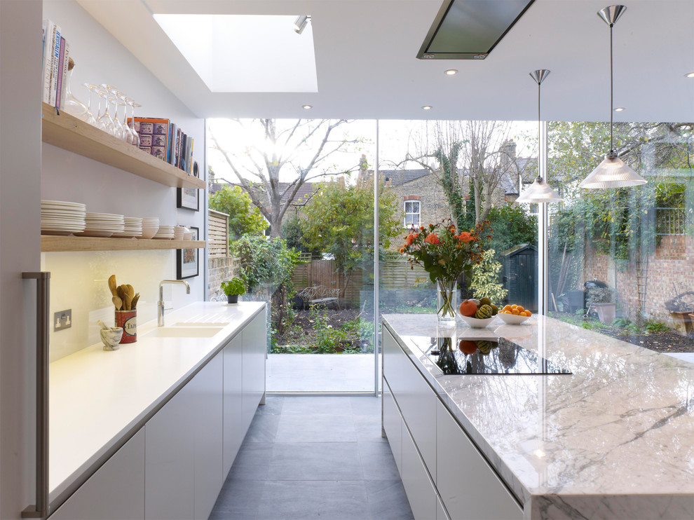 Example of a large trendy galley ceramic tile open concept kitchen design in London with an integrated sink, flat-panel cabinets, gray cabinets, marble countertops, white backsplash, glass sheet backsplash and an island
