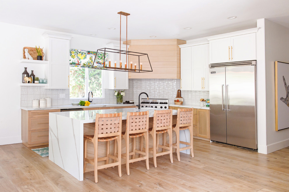 Classic l-shaped kitchen in San Diego with shaker cabinets, white cabinets, white splashback, stainless steel appliances, medium hardwood flooring, an island, brown floors and white worktops.
