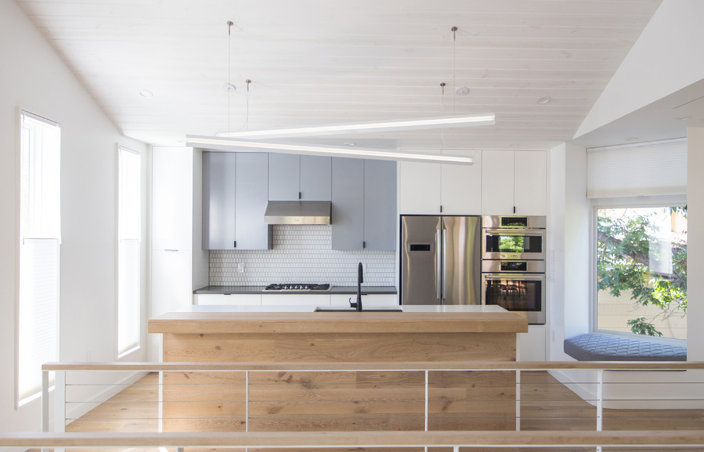 Idéer för ett modernt kök, med släta luckor, grå skåp, vitt stänkskydd, rostfria vitvaror, mellanmörkt trägolv, en köksö, brunt golv, en undermonterad diskho, bänkskiva i kvarts och stänkskydd i keramik