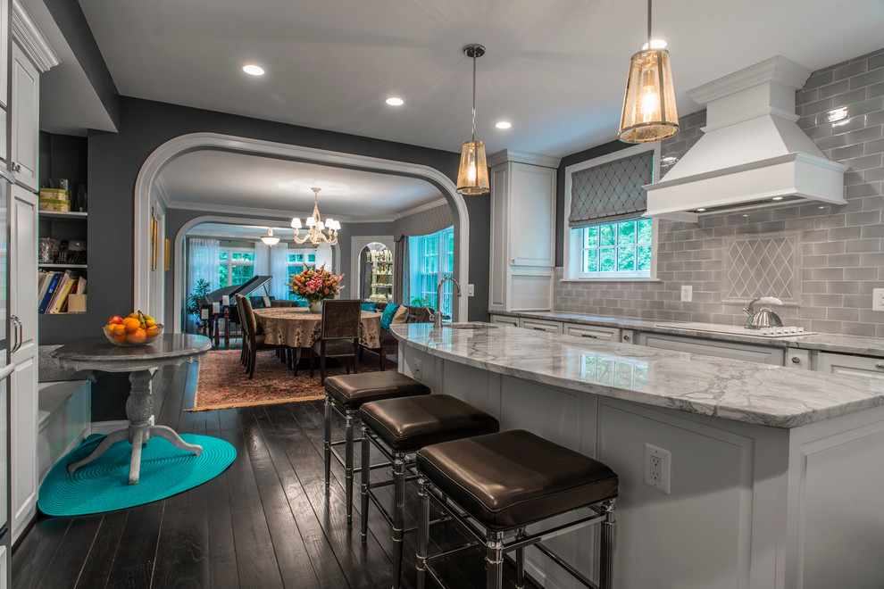 Large transitional u-shaped dark wood floor and brown floor kitchen photo in DC Metro with an undermount sink, raised-panel cabinets, white cabinets, marble countertops, gray backsplash, subway tile backsplash, stainless steel appliances and an island
