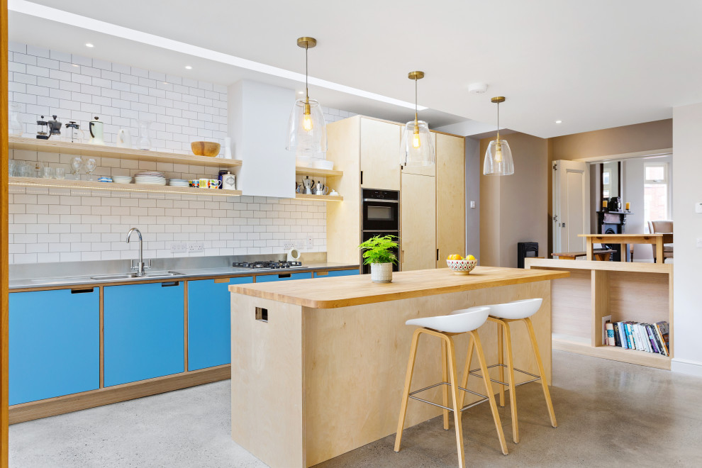 Inspiration for a contemporary single-wall kitchen/diner in Dublin with an integrated sink, flat-panel cabinets, light wood cabinets, stainless steel worktops, white splashback, metro tiled splashback, integrated appliances, concrete flooring, an island, grey floors and grey worktops.
