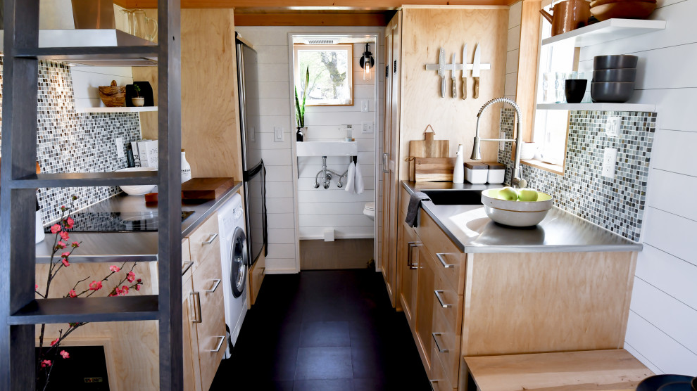 Lantlig inredning av ett litet grå grått kök, med en integrerad diskho, skåp i shakerstil, skåp i ljust trä, bänkskiva i rostfritt stål, grönt stänkskydd, stänkskydd i mosaik, korkgolv och svart golv