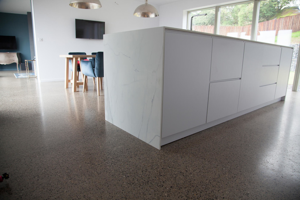 Inspiration for a large modern open plan kitchen in Dublin with a submerged sink, flat-panel cabinets, white cabinets, white splashback, concrete flooring and an island.