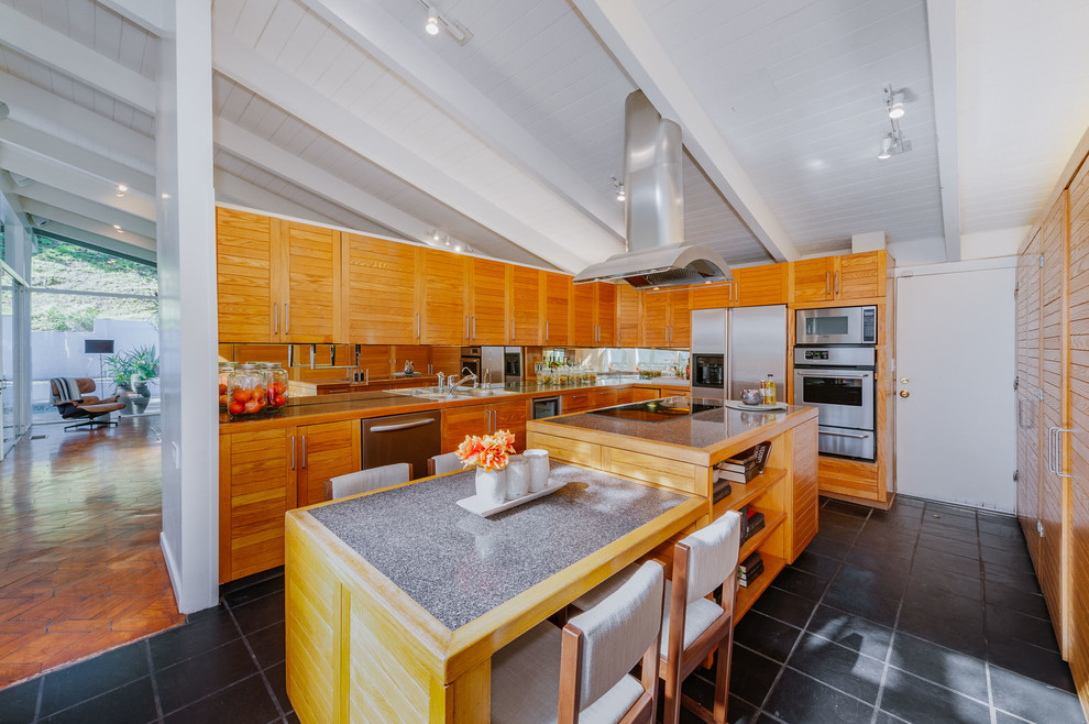 Foto på ett mellanstort 60 tals kök, med rostfria vitvaror, en köksö, grått golv, en dubbel diskho, luckor med lamellpanel, skåp i mellenmörkt trä, spegel som stänkskydd och cementgolv