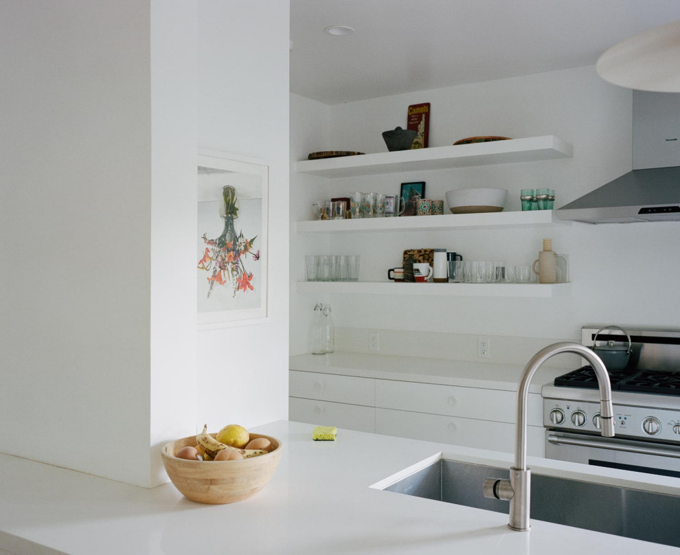 Cette photo montre une cuisine moderne avec un placard à porte plane, une crédence blanche, un électroménager en acier inoxydable, une péninsule et un plan de travail blanc.