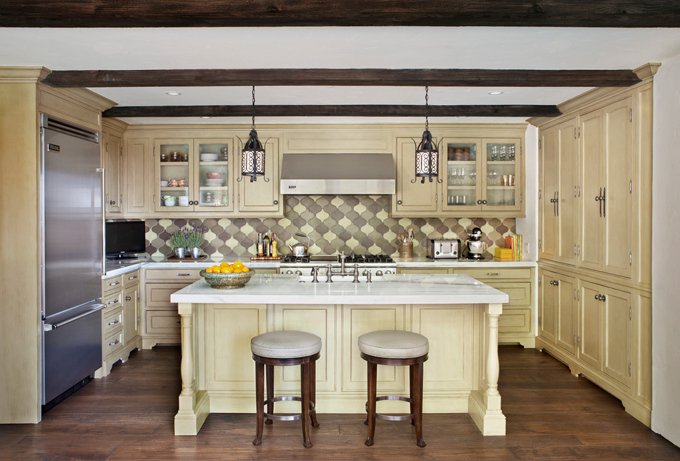 Exempel på ett medelhavsstil l-kök, med marmorbänkskiva, luckor med infälld panel, gula skåp, flerfärgad stänkskydd och rostfria vitvaror