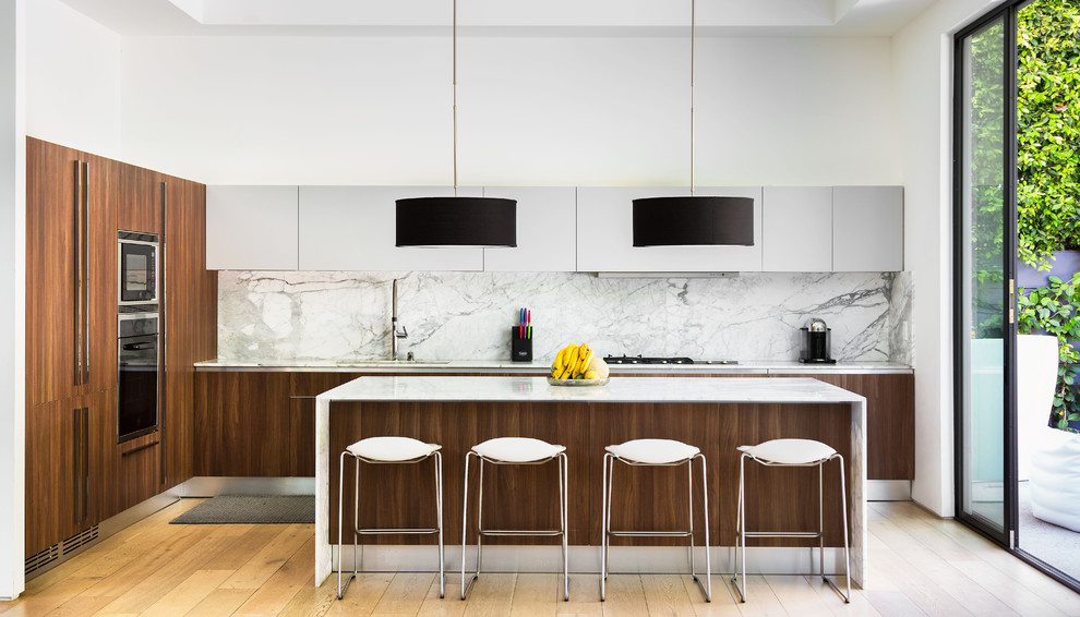 Contemporary l-shaped kitchen in Los Angeles with a submerged sink, flat-panel cabinets, dark wood cabinets, grey splashback, stainless steel appliances, light hardwood flooring, an island and beige floors.