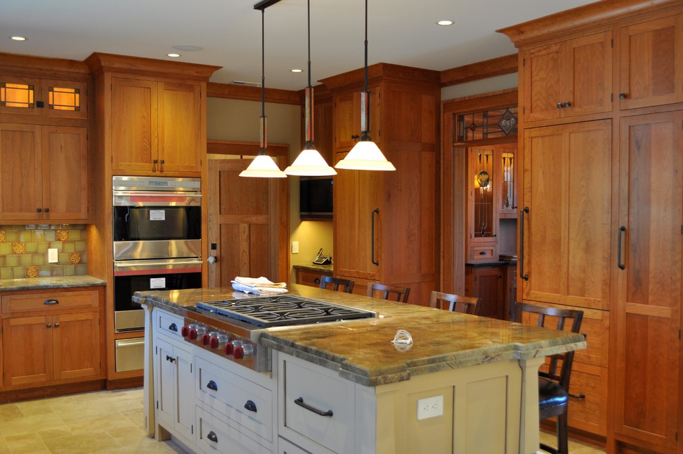 Inredning av ett amerikanskt avskilt, mellanstort l-kök, med luckor med infälld panel, skåp i mellenmörkt trä, grönt stänkskydd, stänkskydd i glaskakel, rostfria vitvaror, en köksö, travertin golv och beiget golv