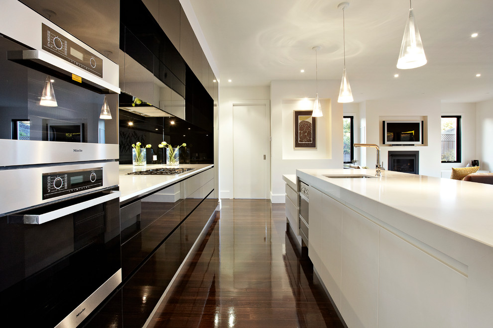 Offene, Zweizeilige Moderne Küche mit Unterbauwaschbecken, flächenbündigen Schrankfronten, weißen Schränken, Küchenrückwand in Schwarz, Küchengeräten aus Edelstahl, dunklem Holzboden und Kücheninsel in Melbourne