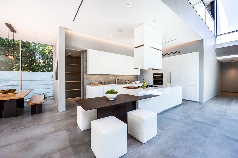 Example of a trendy l-shaped concrete floor and gray floor open concept kitchen design in Los Angeles with flat-panel cabinets, white cabinets, quartzite countertops, white appliances and an island
