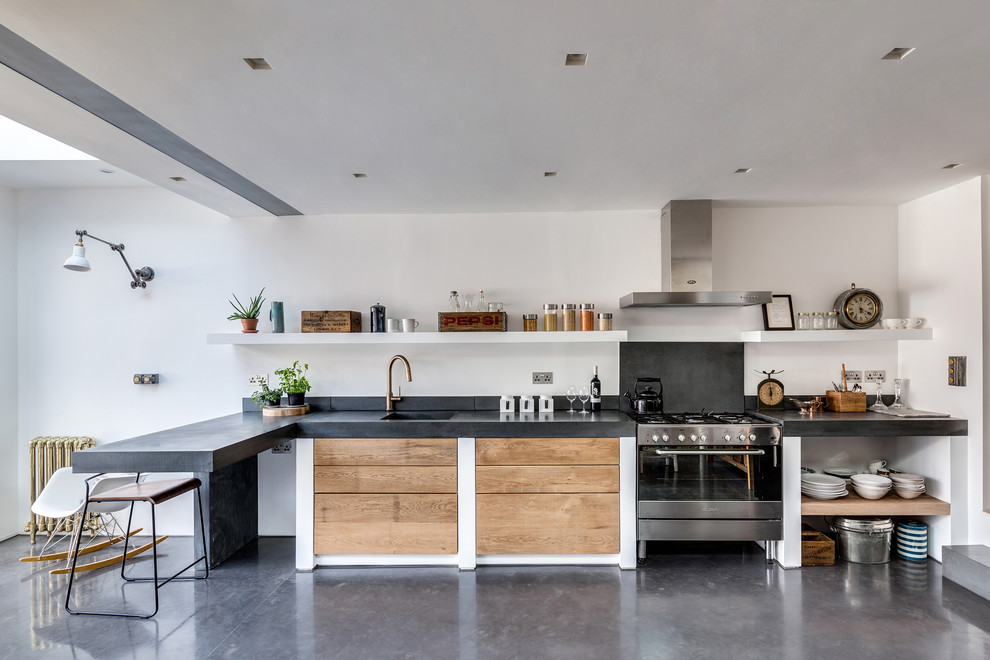 Bild på ett mellanstort funkis l-kök, med en enkel diskho, släta luckor, skåp i ljust trä, bänkskiva i betong, grått stänkskydd, rostfria vitvaror och betonggolv