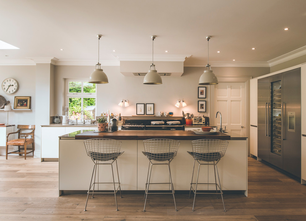 Mid-sized trendy medium tone wood floor and brown floor kitchen photo in Other with flat-panel cabinets, beige cabinets, stainless steel appliances and an island