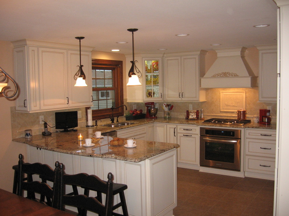 Cette image montre une cuisine américaine traditionnelle en U avec un évier encastré, un placard à porte plane, un plan de travail en granite, une crédence en céramique, un électroménager en acier inoxydable et un sol en bois brun.