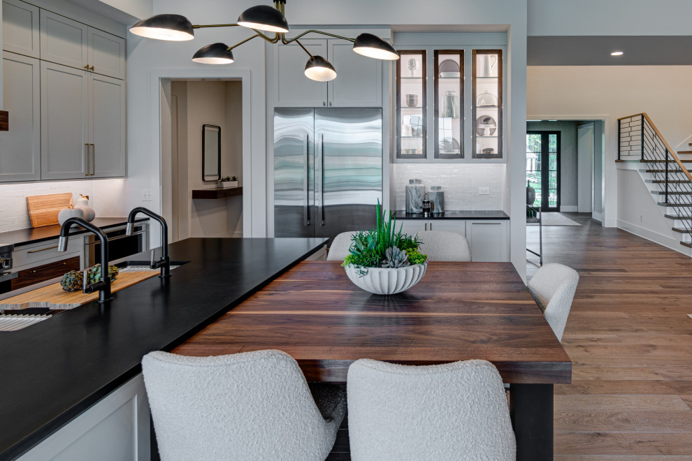Inspiration for a mid-sized contemporary l-shaped light wood floor and brown floor eat-in kitchen remodel in Indianapolis with an undermount sink, shaker cabinets, white cabinets, quartz countertops, white backsplash, ceramic backsplash, stainless steel appliances, an island and black countertops