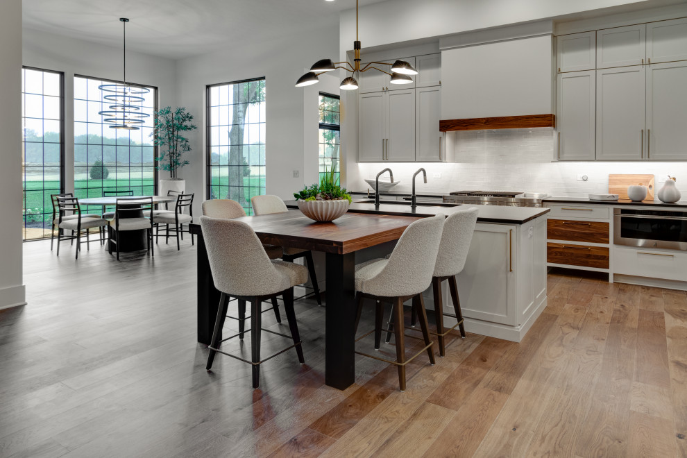Eat-in kitchen - mid-sized contemporary l-shaped light wood floor and brown floor eat-in kitchen idea in Indianapolis with an undermount sink, shaker cabinets, white cabinets, quartz countertops, white backsplash, ceramic backsplash, stainless steel appliances, an island and black countertops