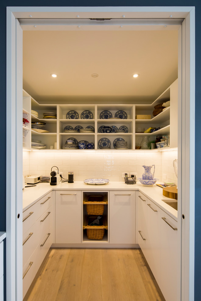Medium sized contemporary u-shaped kitchen pantry in Christchurch with a submerged sink, white cabinets, engineered stone countertops, white splashback, porcelain splashback, light hardwood flooring and grey floors.