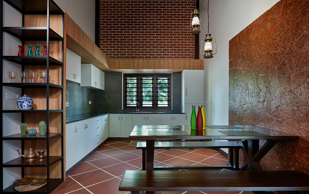 他の地域にある中くらいなトロピカルスタイルのおしゃれなキッチン (フラットパネル扉のキャビネット、白いキャビネット、セラミックタイルの床、赤い床、黒いキッチンカウンター) の写真