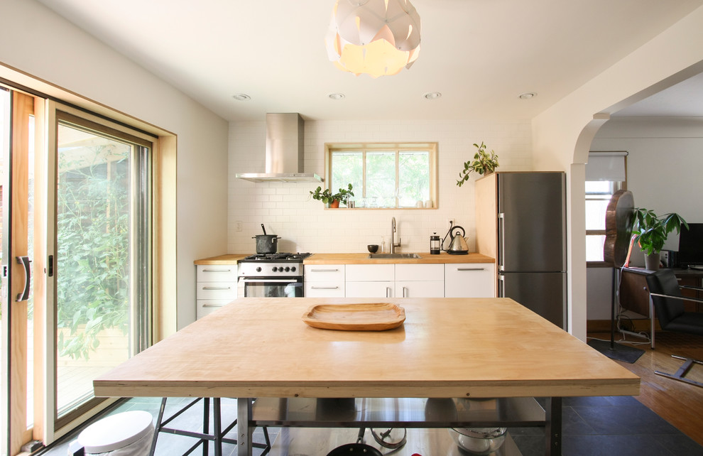 Exempel på ett skandinaviskt linjärt kök med öppen planlösning, med träbänkskiva, rostfria vitvaror, en köksö, en enkel diskho, vita skåp och vitt stänkskydd