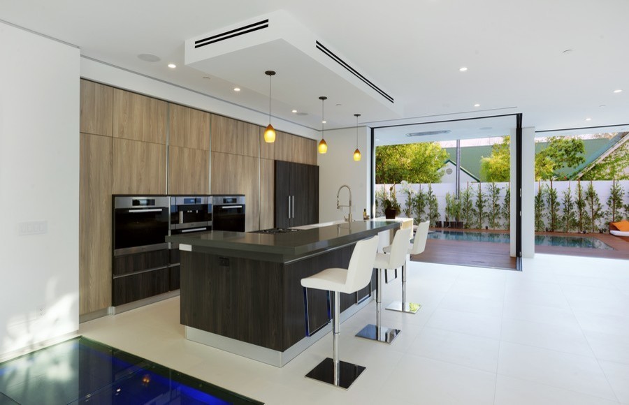 Example of a mid-sized minimalist u-shaped ceramic tile eat-in kitchen design in Los Angeles with a farmhouse sink, flat-panel cabinets, light wood cabinets, limestone countertops, white backsplash, limestone backsplash, stainless steel appliances and an island
