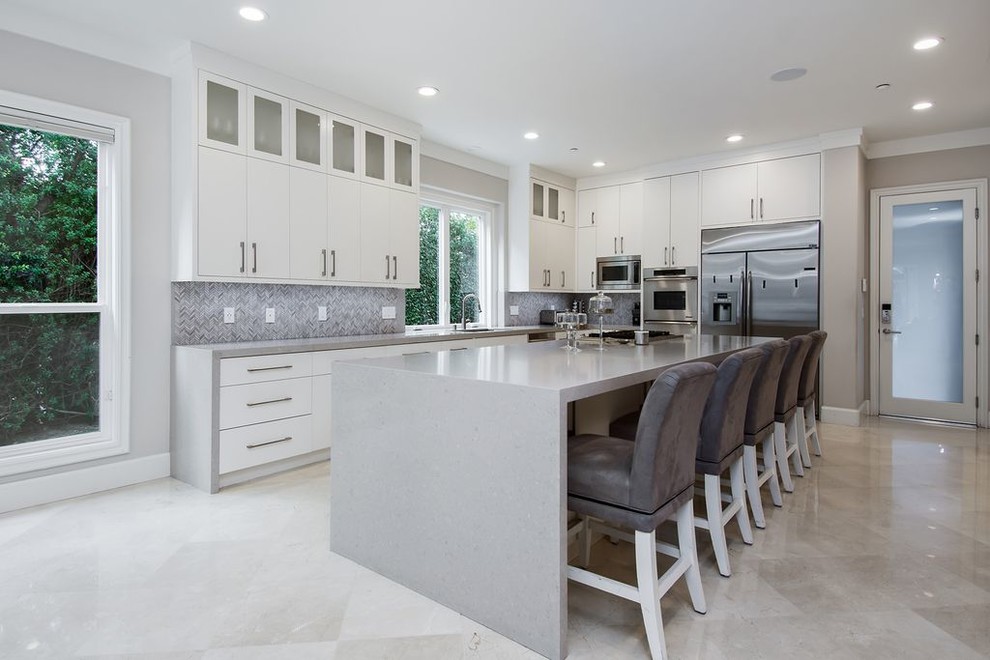 Example of a mid-sized trendy l-shaped porcelain tile and beige floor eat-in kitchen design in Los Angeles with an undermount sink, flat-panel cabinets, white cabinets, quartz countertops, gray backsplash, stone tile backsplash, stainless steel appliances, an island and gray countertops