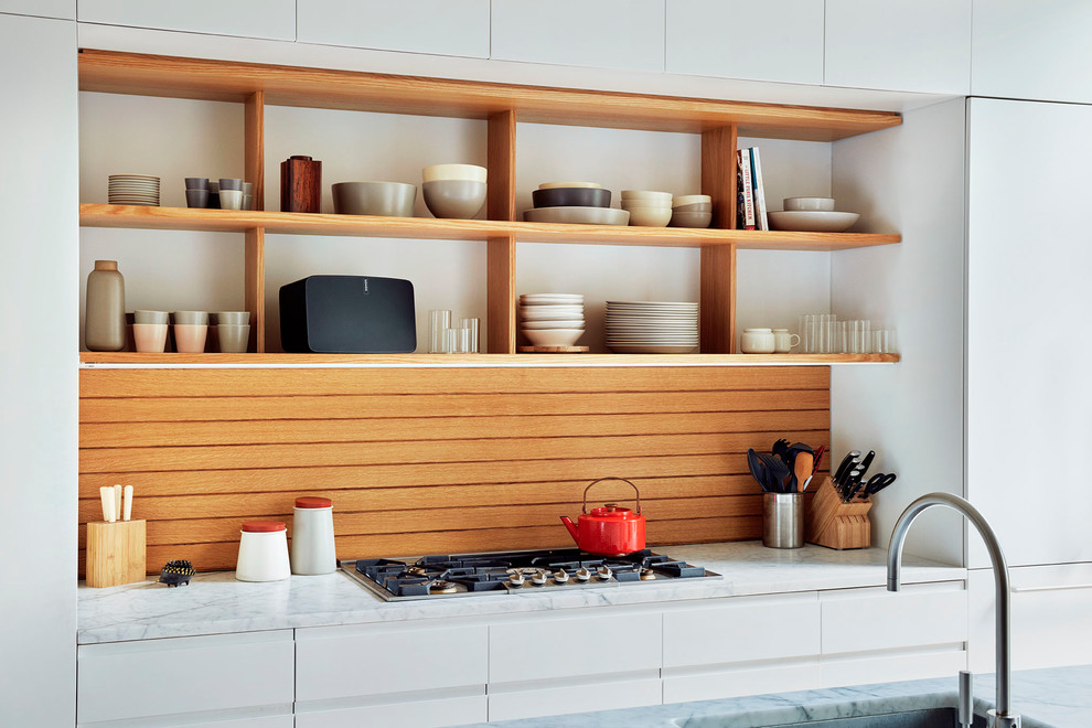 Bild på ett mellanstort, avskilt minimalistiskt parallellkök, med en undermonterad diskho, släta luckor, vita skåp, marmorbänkskiva, brunt stänkskydd, stänkskydd i trä, en köksö och integrerade vitvaror