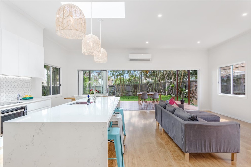 Inspiration for a large contemporary galley open plan kitchen in Gold Coast - Tweed with a submerged sink, flat-panel cabinets, white cabinets, quartz worktops, white splashback, ceramic splashback, coloured appliances, medium hardwood flooring, an island and brown floors.