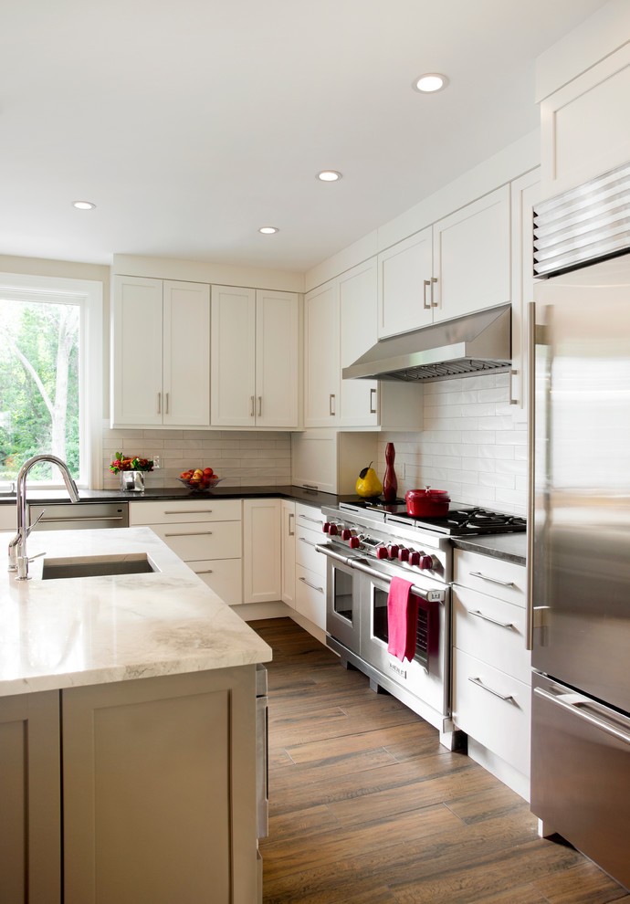 Eat-in kitchen - large transitional u-shaped eat-in kitchen idea in Boston with a single-bowl sink, recessed-panel cabinets, white cabinets, granite countertops, white backsplash, ceramic backsplash, stainless steel appliances and an island
