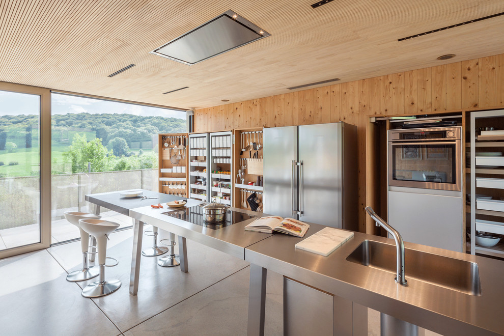 Idées déco pour une cuisine parallèle moderne en bois brun avec un évier intégré, un placard sans porte, un plan de travail en inox, sol en béton ciré, îlot, un sol gris et un plan de travail gris.