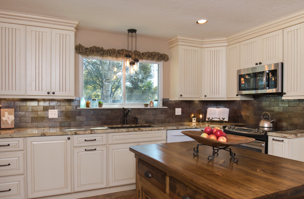 Photo of a large country u-shaped kitchen in Houston with beaded cabinets, granite worktops, a submerged sink, white cabinets, brown splashback, metro tiled splashback, stainless steel appliances, an island, brown floors and ceramic flooring.