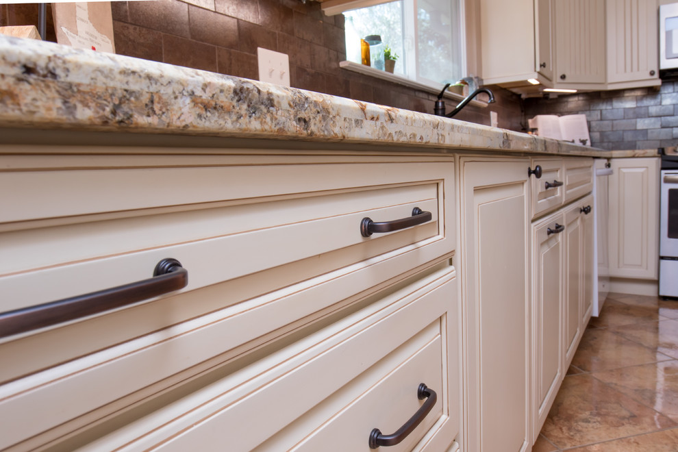 Exempel på ett stort lantligt u-kök, med luckor med profilerade fronter, granitbänkskiva, en undermonterad diskho, vita skåp, brunt stänkskydd, stänkskydd i tunnelbanekakel, rostfria vitvaror, klinkergolv i keramik, en köksö och brunt golv