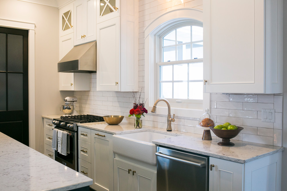 Mid-sized farmhouse l-shaped brown floor and dark wood floor kitchen pantry photo in Other with a farmhouse sink, white cabinets, quartz countertops, white backsplash, stainless steel appliances, an island, recessed-panel cabinets, subway tile backsplash and white countertops