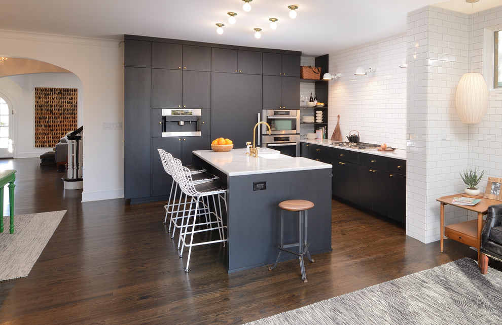 Transitional l-shaped dark wood floor and brown floor kitchen photo in Chicago with a farmhouse sink, flat-panel cabinets, black cabinets, white backsplash, subway tile backsplash, stainless steel appliances and an island