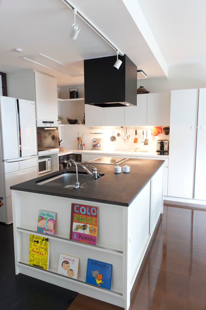 Medium sized contemporary l-shaped kitchen/diner in Tokyo with flat-panel cabinets, white cabinets, white appliances, an island, a submerged sink, white splashback, dark hardwood flooring and brown floors.