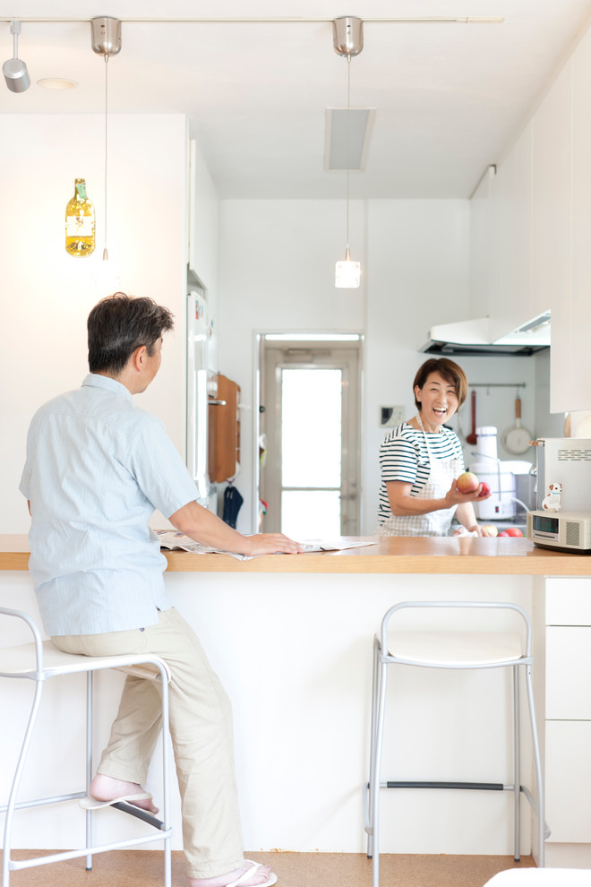 東京23区にある中くらいなおしゃれなキッチン (一体型シンク、フラットパネル扉のキャビネット、白いキャビネット、ステンレスカウンター、白いキッチンパネル、白い調理設備、セラミックタイルの床、アイランドなし) の写真