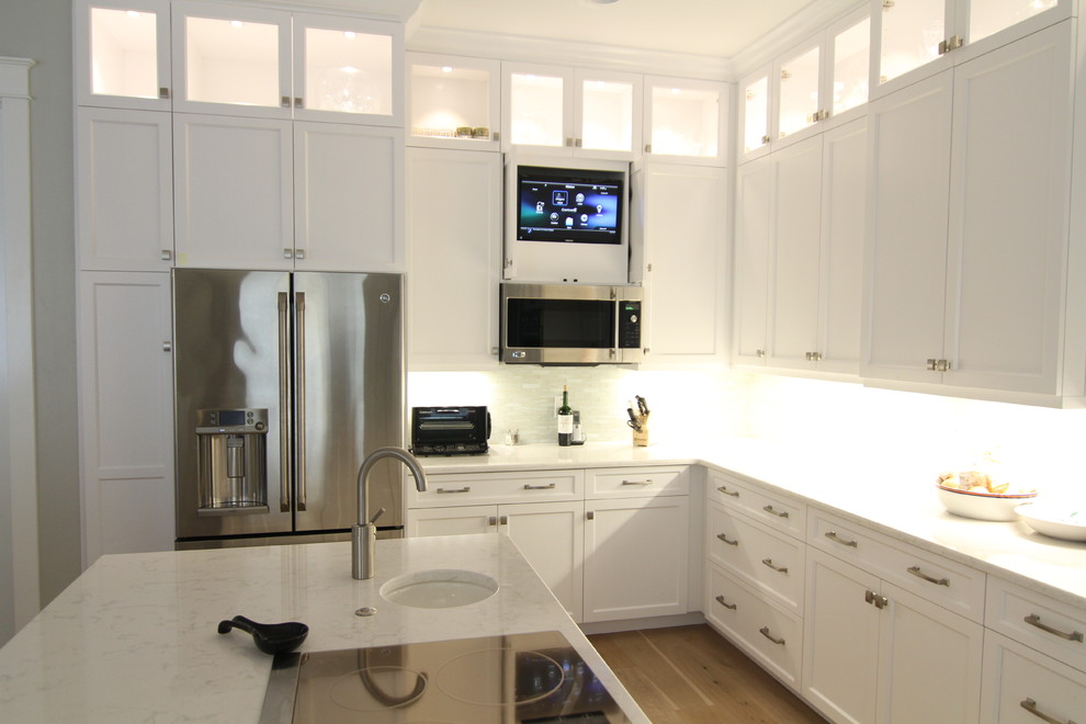 Example of a mid-sized transitional l-shaped medium tone wood floor and brown floor kitchen design in Tampa with an undermount sink, shaker cabinets, white cabinets, quartzite countertops, white backsplash, glass tile backsplash, stainless steel appliances and an island