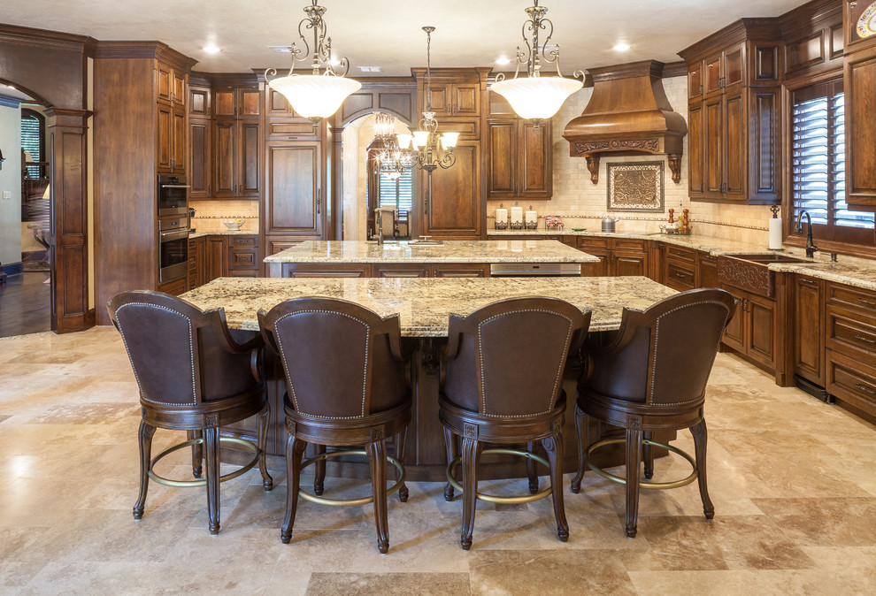 Eat-in kitchen - huge traditional l-shaped travertine floor eat-in kitchen idea in Houston with a farmhouse sink, raised-panel cabinets, medium tone wood cabinets, granite countertops, beige backsplash, stone tile backsplash, paneled appliances and two islands
