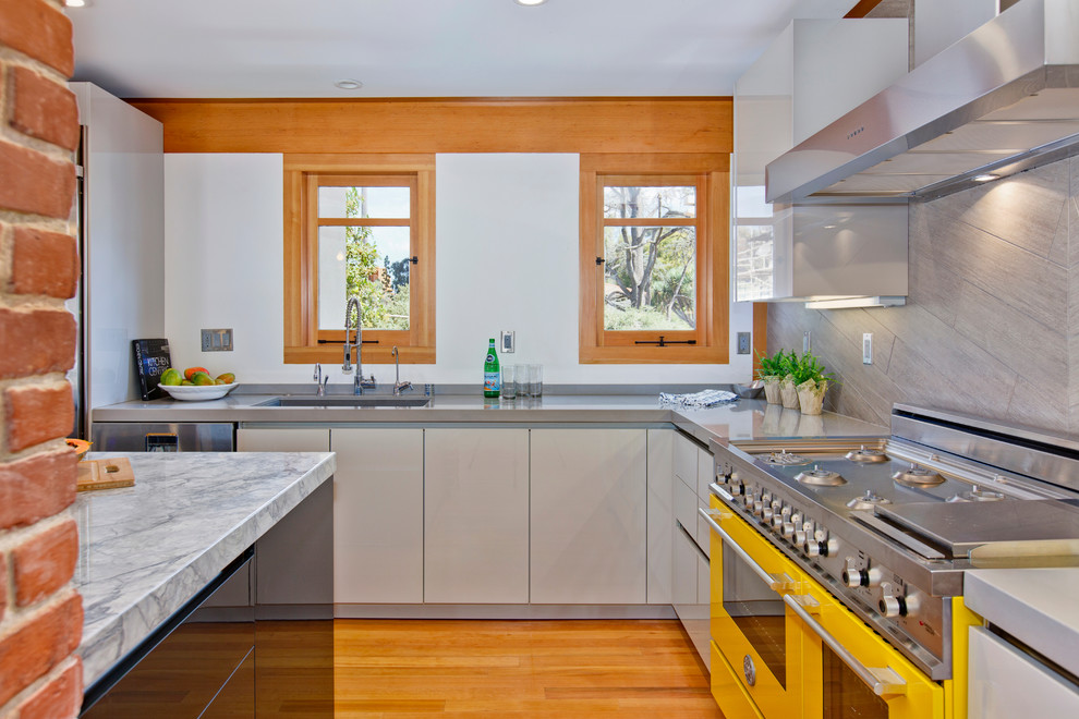 Exempel på ett mellanstort modernt kök, med en undermonterad diskho, släta luckor, grå skåp, bänkskiva i kvarts, grått stänkskydd, stänkskydd i porslinskakel, färgglada vitvaror, mellanmörkt trägolv och en köksö