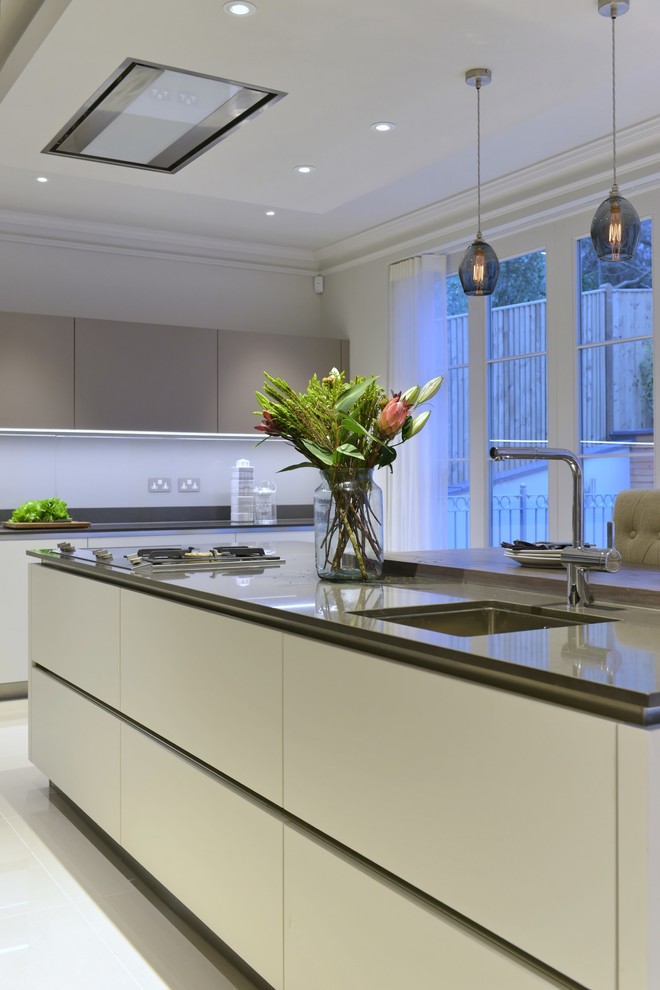 This is an example of a medium sized contemporary l-shaped kitchen/diner in Gloucestershire with a submerged sink, flat-panel cabinets, white cabinets, composite countertops, white splashback, glass sheet splashback, stainless steel appliances, porcelain flooring and an island.