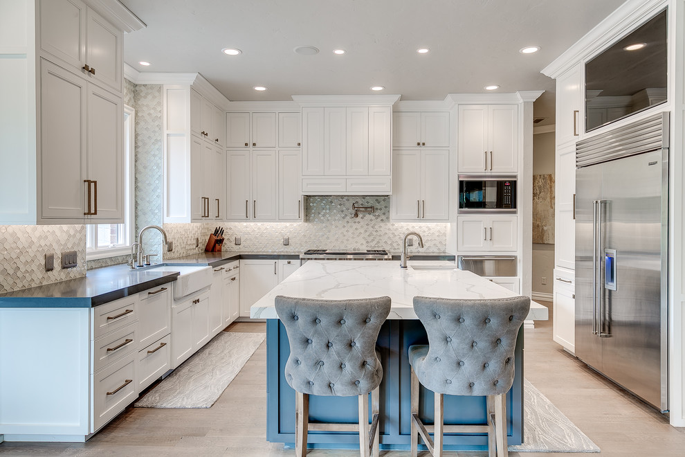 Large transitional l-shaped light wood floor enclosed kitchen photo in Nashville with a farmhouse sink, recessed-panel cabinets, white cabinets, quartz countertops, gray backsplash, metal backsplash, stainless steel appliances and an island